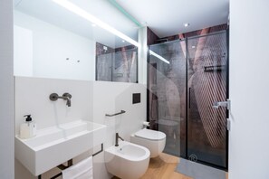 Un baño moderno con cabina de ducha de vidrio, un lavabo blanco y un bidé.