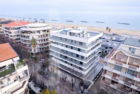 Un hotel de varios pisos con balcones, vista a la playa y zona de estacionamiento.
