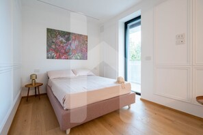 Un dormitorio con cama, mesita de noche, lámpara y ventana.