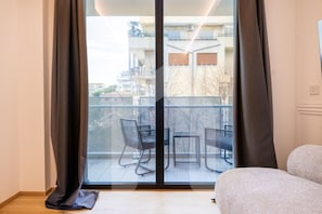 Una habitación con un amplio ventanal corredera que da a un balcón exterior con dos sillas y una mesa.