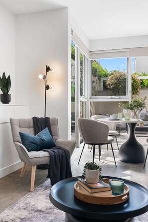 Un salón moderno con sofá, sillón y mesa de centro, con una planta en maceta, libros y un objeto decorativo.