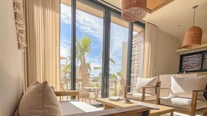 A modern living room with a sofa, chairs, a coffee table, and a view of palm trees and the ocean.