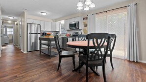 A modern kitchen with white cabinets, stainless steel appliances, and a dining area with a round table and chairs. - 4 bedroom, King Bed, 4 min to Fairgrounds, TVs in all Rooms (Perry)