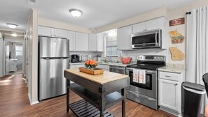 A modern kitchen with stainless steel appliances, white cabinetry, and a wooden table with a vase of flowers. - 4 bedroom, King Bed, 4 min to Fairgrounds, TVs in all Rooms (Perry)