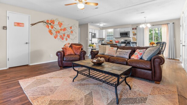 A living room with a brown leather sofa, a coffee table, and a ceiling fan. - 4 bedroom, King Bed, 4 min to Fairgrounds, TVs in all Rooms (Perry)
