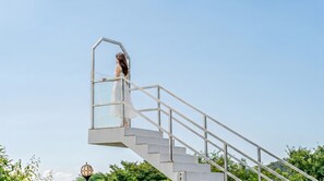 A person on a white staircase with a glass enclosure, surrounded by greenery. - Yeosu Everyday Small Changes Pension (Yeosu)