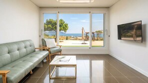 A modern living room with a green sofa, a wooden coffee table, and a large window offering a view of a beach and ocean. - Yeosu Everyday Small Changes Pension (Yeosu)