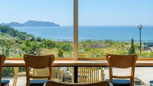 A view from a room with large windows overlooking a coastal landscape, featuring a table and chairs.
