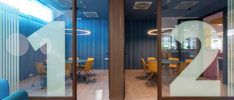 A modern office space with glass partitions, a conference area with tables and chairs, and a staircase.
