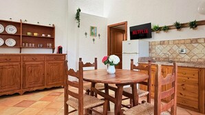 A kitchen with wooden cabinets, a dining table with chairs, a TV on the wall, and a flower vase. - [Lauro]Apartment in the middle of the greenery (Orosei)