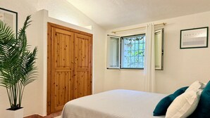 A bedroom with a bed, a window with curtains, a wooden wardrobe, and a potted plant. - [Lauro]Apartment in the middle of the greenery (Orosei)