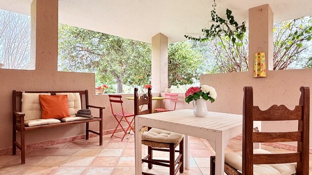 A patio with a wooden table, chairs, and a bench. There is a potted plant with flowers and a vase on the table. - [Lauro]Apartment in the middle of the greenery (Orosei)