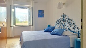 Un dormitorio con cama, ventana, un cuadro y mesita de noche.
