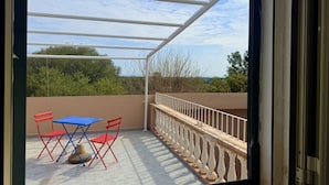 Un balcón con mesa y sillas, baranda y vista a árboles y cielo.