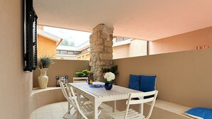 A white table and chairs set on a balcony with a stone pillar, a vase with flowers, and a blue cushion. - [Leccio] Comfort and Nature in Orosei (Orosei)