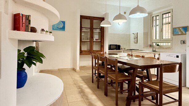 A dining area with a wooden table and chairs, a white curved bench, and pendant lights. - [Leccio] Comfort and Nature in Orosei (Orosei)