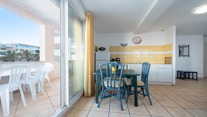 A balcony with a table and chairs, a kitchen area with yellow tiles, and a view of buildings. - Bright apt with large balcony for 4 pers (Agde)