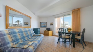 A living room with a sofa, a TV, a table with chairs, and a balcony with curtains. - Bright apt with large balcony for 4 pers (Agde)
