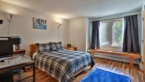 A bedroom with a bed, a bench, a heater, a TV, and a ski-themed wall decoration. - The Powder Pad Studio - Perfect for Two - On Shuttle Route w/ Amenities A4A (Killington)