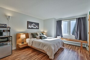 A bedroom with a bed, bedside table, lamp, and a window with curtains.