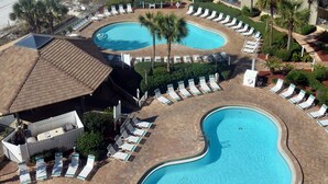 Ein Hotel mit mehreren Balkonen mit Blick auf einen Strand und einen Poolbereich mit Liegestühlen und Palmen.