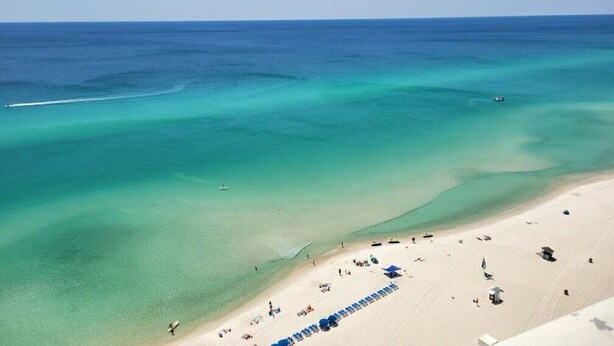 Ein Strand mit klarem türkisblauem Wasser, einem sandigen Ufer und einigen Strandsonnenschirmen.
