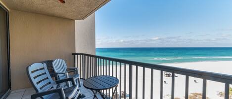 A balcony with a view of the beach, a table, and two chairs.