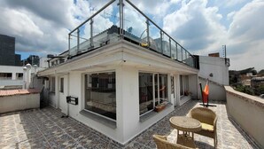 Une terrasse sur le toit dotée d'une balustrade en verre, d'un espace salon avec des meubles en osier et d'un foyer.