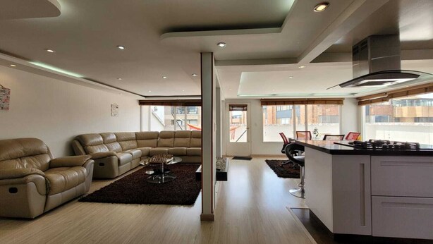 Un salon moderne avec un canapé d’angle, une table basse et un coin cuisine équipé d’une cuisinière.