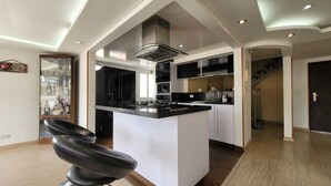 Une cuisine moderne dotée d’un îlot central, de plans de travail noirs et d’appareils électroménagers en acier inoxydable. On aperçoit, au premier plan, une vitrine contenant des bouteilles et un fauteuil en cuir noir.