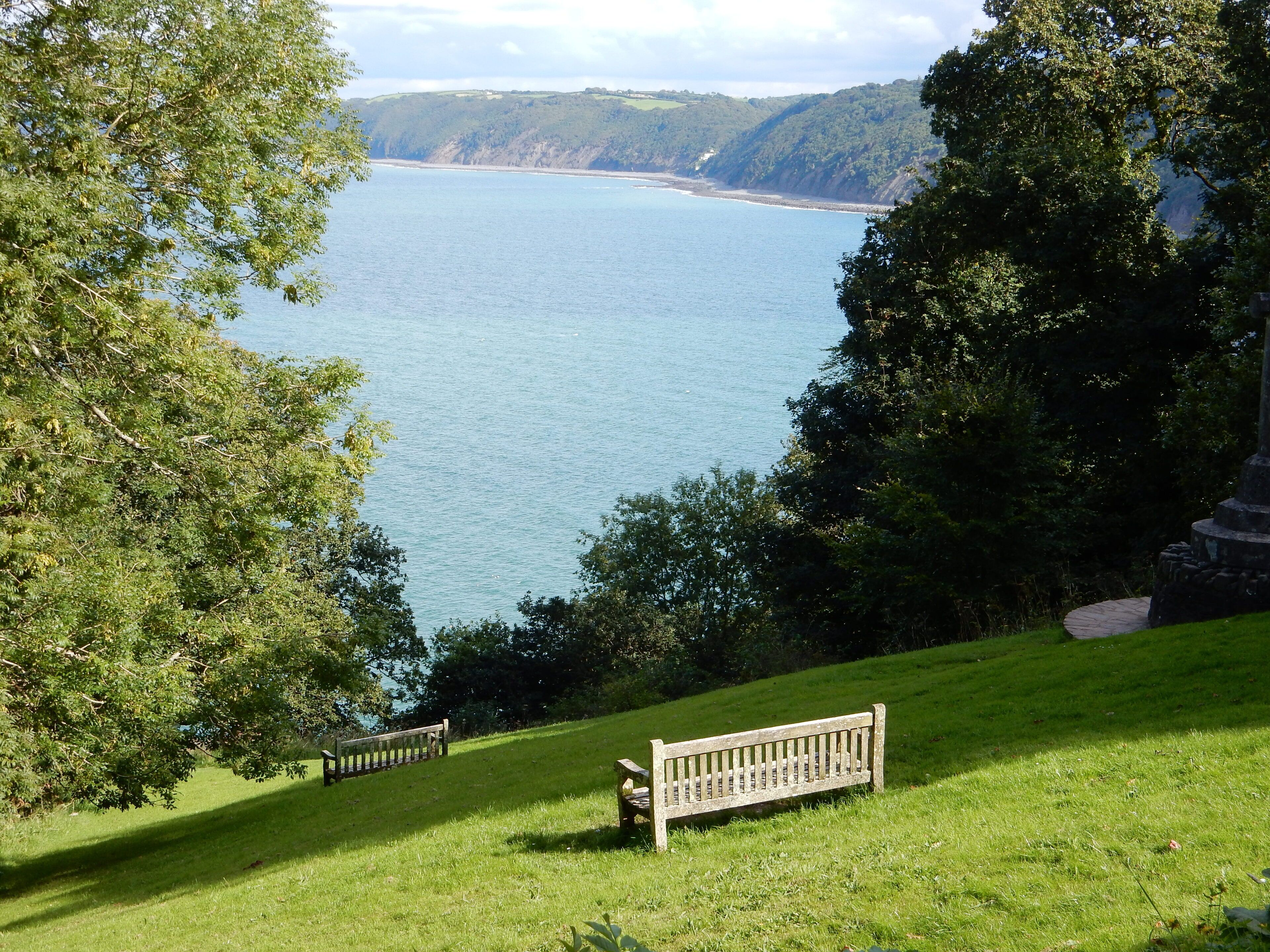 A grassy area with two benches overlooking a body of water and a hilly landscape.
