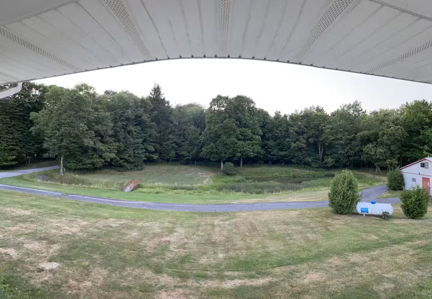 Blick auf eine Wiese mit einer Straße, Bäumen und einem kleinen Gebäude.