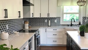 Een moderne keuken met witte kastjes, een zwart-wit betegelde achterwand, een houten vloer en een raam met uitzicht op groen.