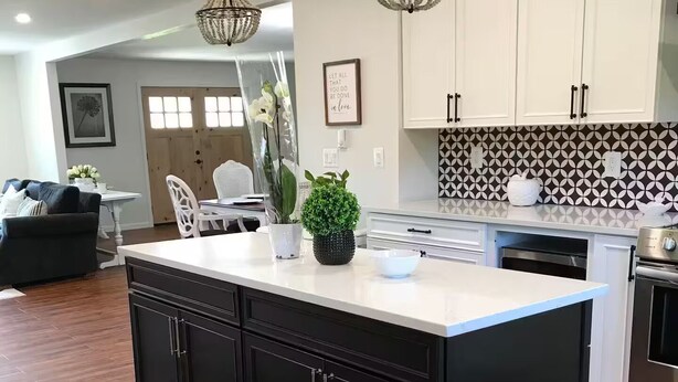 Een moderne keuken met een centraal eiland, zwarte kasten, witte aanrechtbladen en een decoratieve spatwand.