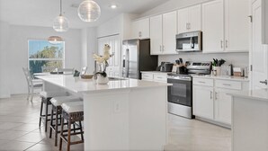 Une cuisine moderne avec des meubles blancs, des appareils en acier inoxydable et un îlot central doté de tabourets de bar.