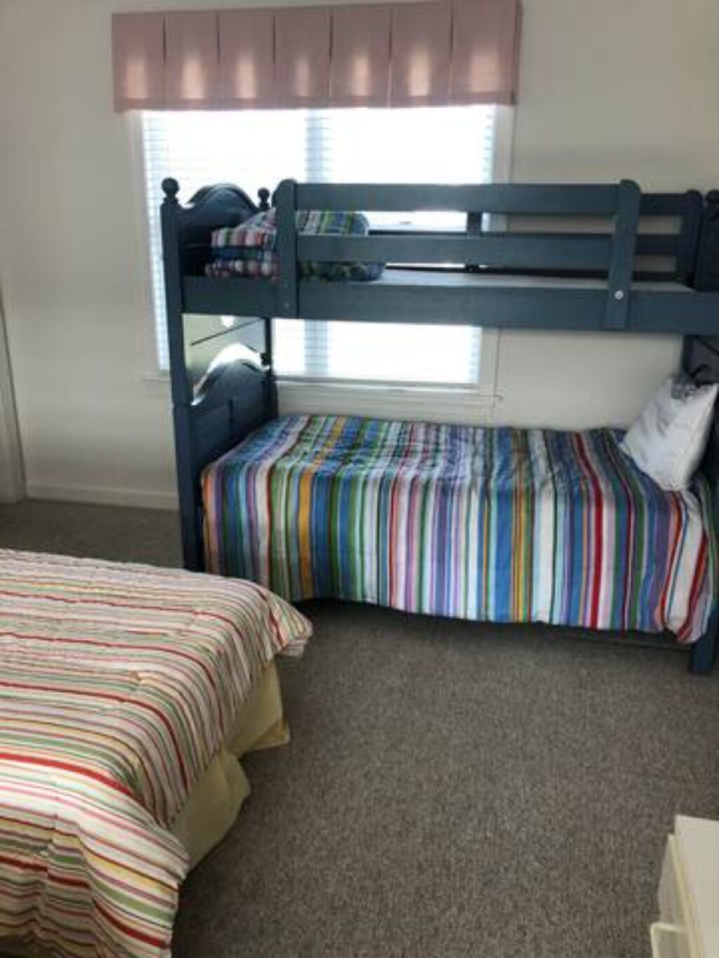 A bunk bed room with striped bedding and a window with blinds.