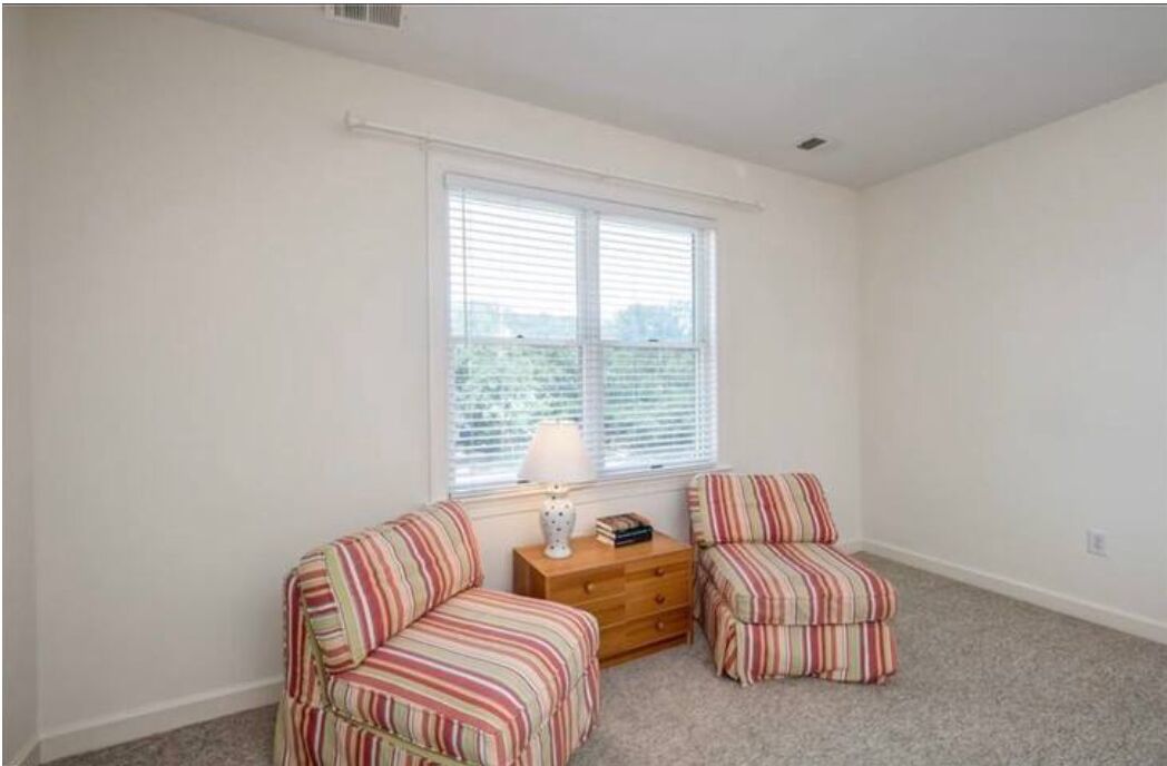 A room with two striped armchairs, a small wooden dresser, and a window with blinds.