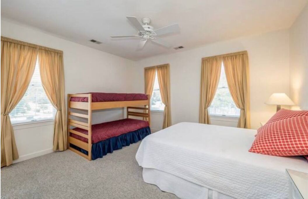 A room with a bunk bed, a single bed, a ceiling fan, and windows with curtains.