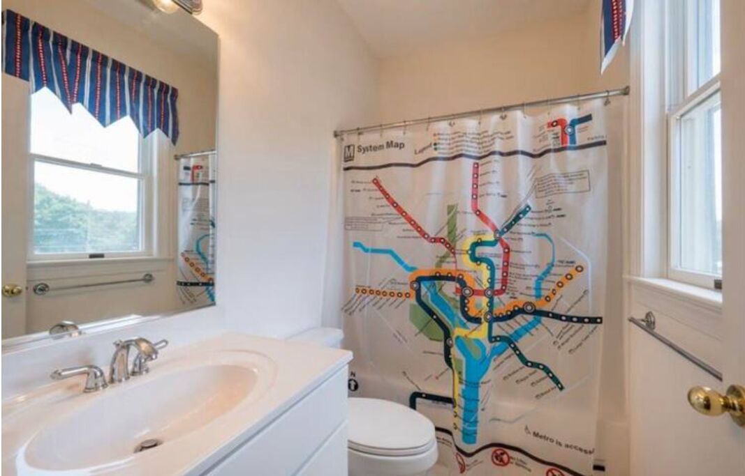 A bathroom with a white sink, toilet, and a shower curtain featuring a subway map design.