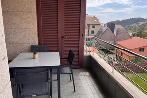 A balcony with a table and chairs, a closed door, and a view of buildings and a hill.