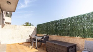 Un patio exterior con una mesa, sillas, un banco de almacenamiento y una pared de setos.
