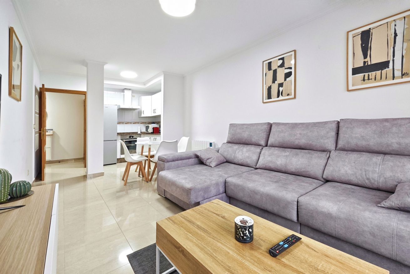 Een moderne woonkamer met een grijze modulaire bank, een houten salontafel en een afstandsbediening.