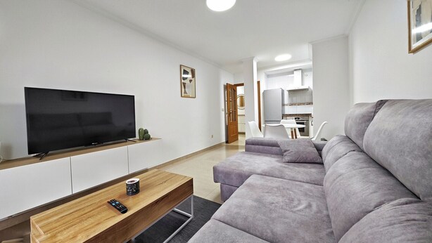 Una sala de estar moderna con un televisor de pantalla plana, una mesa de centro de madera y un sofá gris.