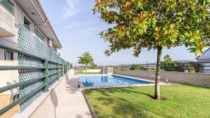 Una piscina con superficie de agua azul cristalina, rodeada por un césped cuidado y una valla de metal verde.