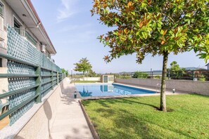 Un área de piscina con cielo despejado, césped y un edificio con balcón.