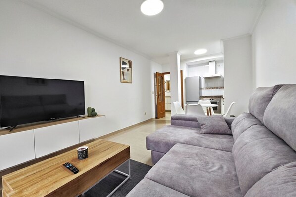 A modern living room with a flat-screen TV, a wooden coffee table, and a grey sofa.