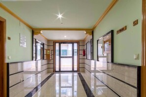 Corredor com piso lustroso, portas identificadas com letras e extintor de incêndio na parede.