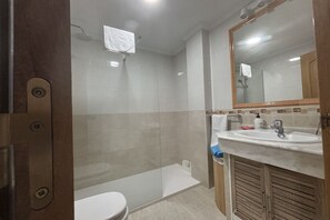 Un baño con ducha, inodoro, lavamanos y espejo.