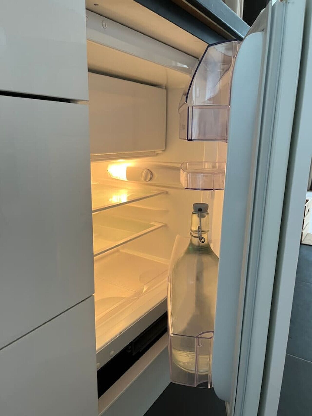An open refrigerator with clear shelves and a water dispenser.