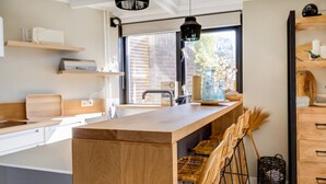 Een moderne keuken met een centraal eiland, barkrukken, houten kastjes en een hangende lamp.